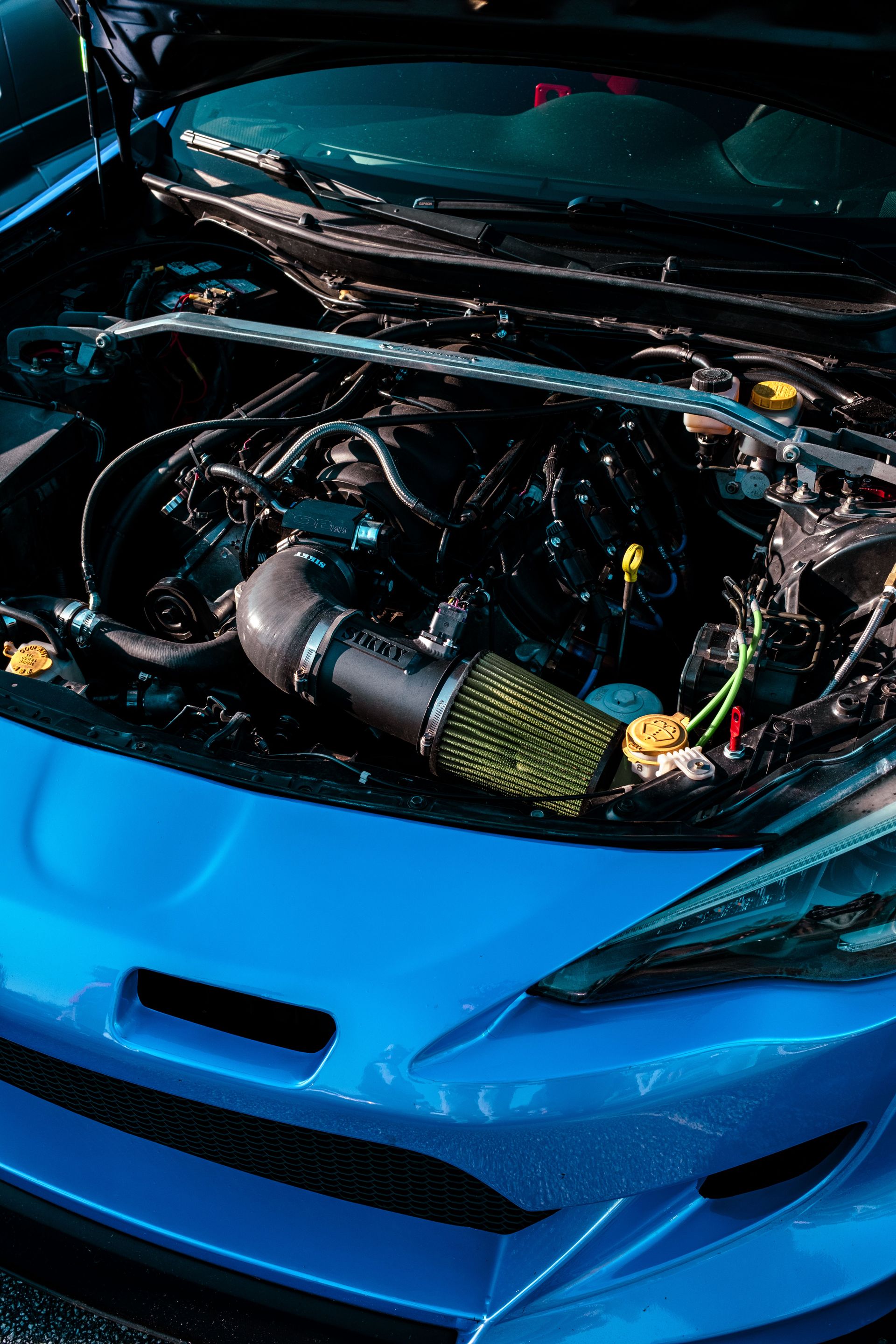 Detailed photo of a blue car's engine showcasing intricate mechanical components under natural light.