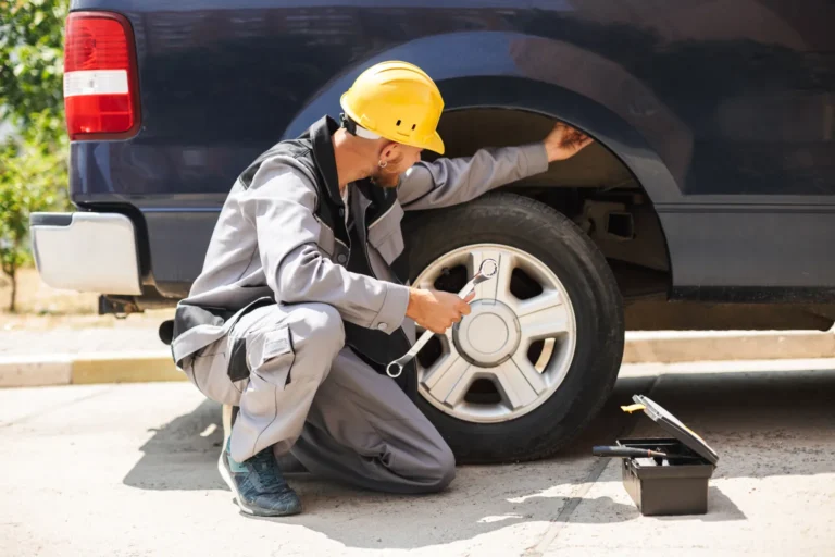 Young mechanic work clothes yellow hardhat using wrench changing car wheel outdoor